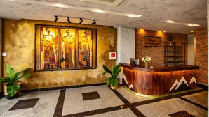 A reception area with a wooden reception desk, a large wall mural, and a brick wall. - Bed Station Hostel (Quy Nhon)