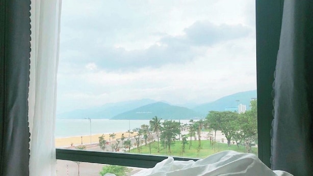 A bed with a view of a beach and mountains through a window. - Bed Station Hostel (Quy Nhon)