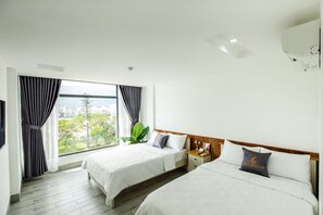 A hotel room with two beds, a large window with curtains, a wooden headboard, and a nightstand with a lamp.