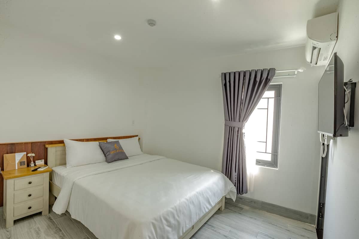 A bedroom with a bed, nightstand, and a window with curtains.