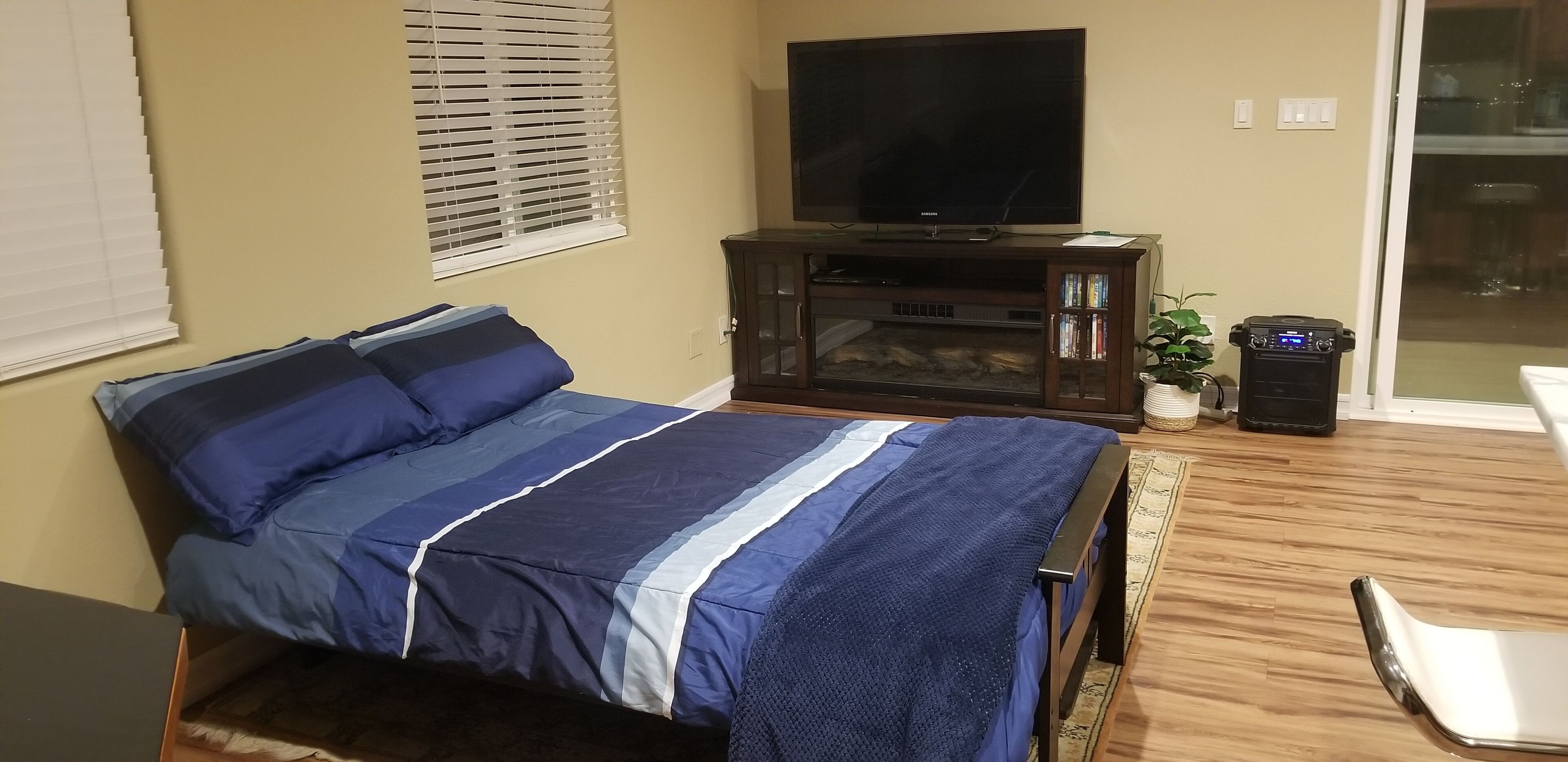 Quarto com uma cama, televisão sobre um suporte, um pequeno armário e uma planta.
