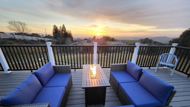 Una terrazza con sedute imbottite blu e un tavolo centrale dotato di elemento decorativo a fuoco, affacciata su un panorama mozzafiato al tramonto.