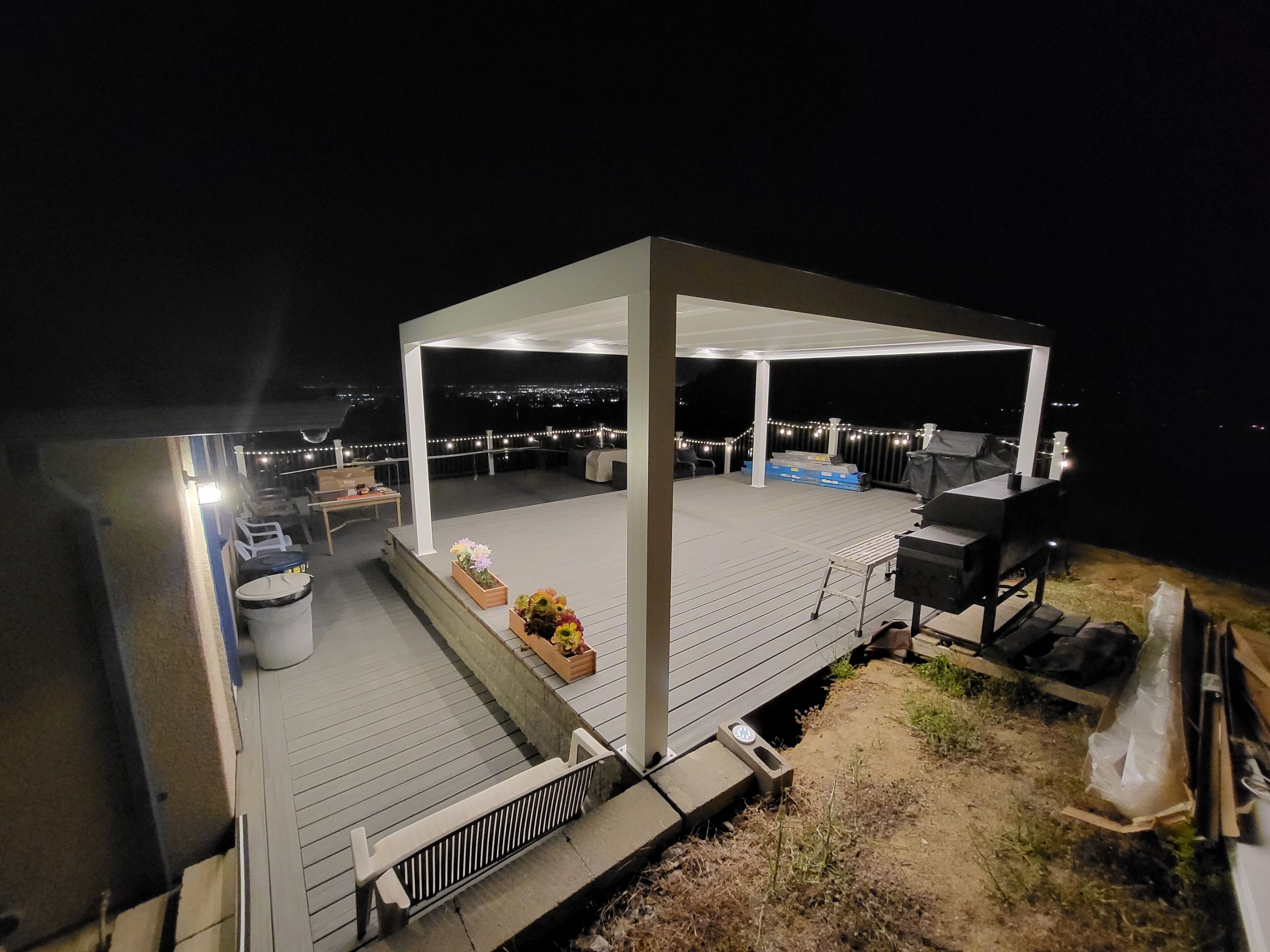 Une terrasse extérieure couverte, dotée d’un barbecue et d’un espace salon, offrant une vue sur le paysage urbain illuminé la nuit.