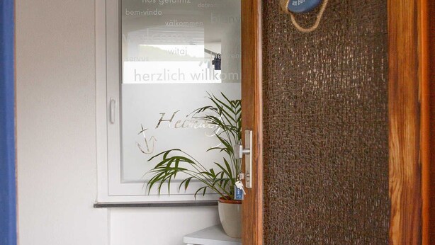 A wooden door with a life preserver decoration, a white door frame, and a potted plant on the wall.
