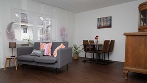 A modern living room with a grey sofa, wooden floor, and a dining area with a table and chairs.