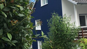 A two-story house with a dark blue exterior and white trim, surrounded by greenery. - Ferienwohnung West - Ferienwohnungen Heimathafen (Edertal)