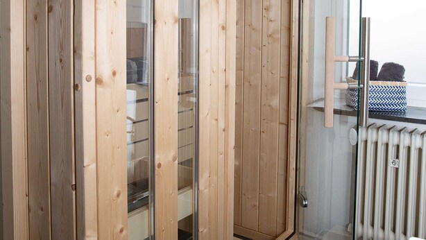 A wooden wardrobe with glass doors, a glass shower enclosure, and a radiator. - Ferienwohnung West - Ferienwohnungen Heimathafen (Edertal)