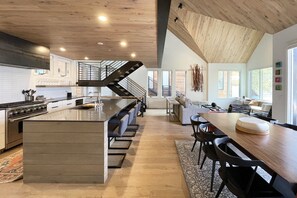 A modern kitchen with a central island, a dining area with a long table, and a staircase leading to an upper level. - Modern Luxury Loft | Gym & Sauna, Steps to Gondola, Main St & Downtown Telluride (Telluride)