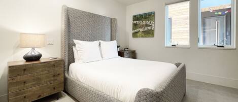 A bedroom with a bed, a dresser, a lamp, and two windows.