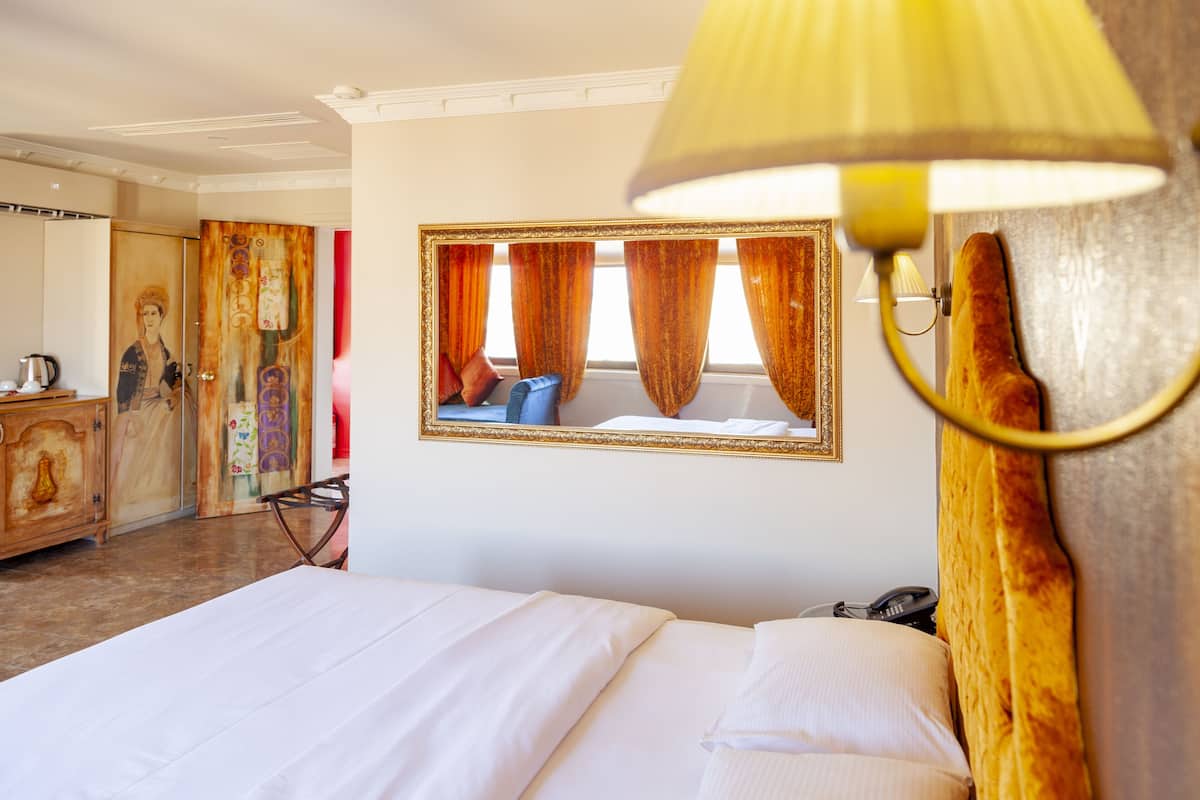 A hotel room with a bed, a mirror, a lamp, a telephone, and a wardrobe.