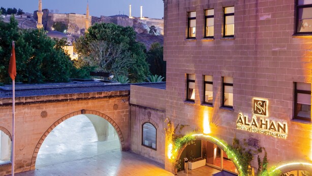 A hotel with a prominent sign, a stone archway, and a view of a historic building in the background. - Ala Han Boutique Hotel (Sanliurfa)