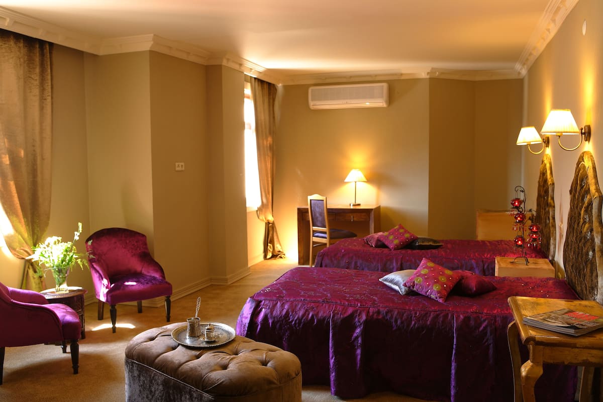 A hotel room with a large bed, two chairs, a small table, and a lamp.