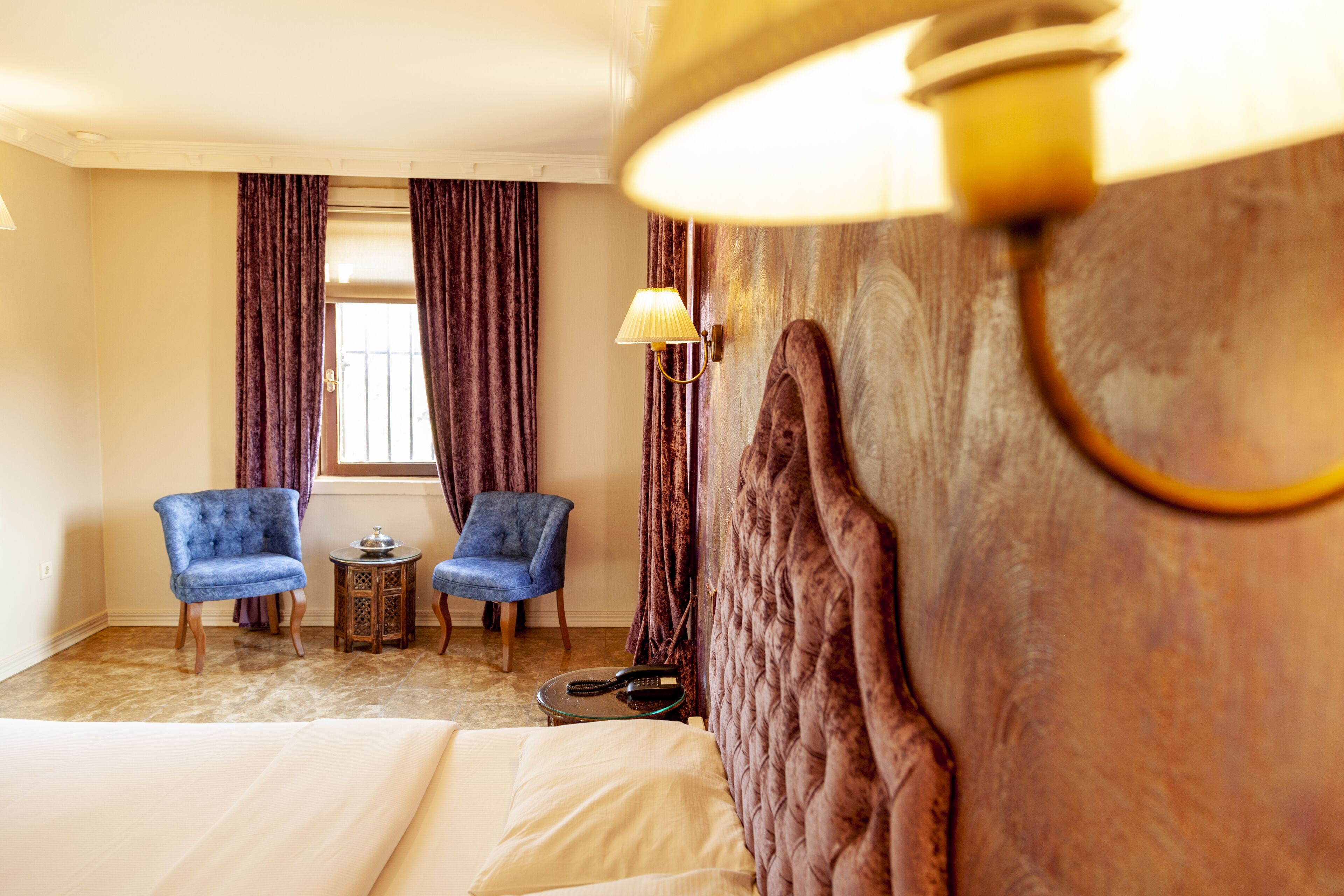 A hotel room with a bed, two armchairs, a small table with a lamp, and a window with curtains.