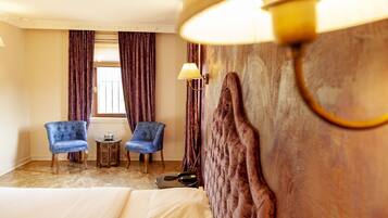 A hotel room with a bed, two armchairs, a small table with a lamp, and a window with curtains.