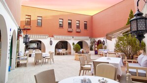An outdoor dining area with tables and chairs, a fountain, and a building with arched windows in the background. - Ala Han Boutique Hotel (Sanliurfa)