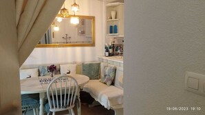 Un coin repas accueillant avec une table blanche, des chaises et un banc. Un lustre est suspendu au-dessus de la table et un miroir est accroché au mur.