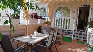 Une terrasse extérieure avec une table et des chaises, un pot de fleurs et une vue sur l’intérieur.