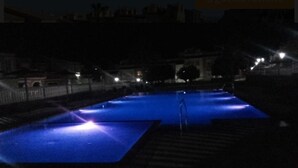 Vue nocturne d’une piscine à la surface bleue, entourée d’un mur de briques et d’une rambarde.