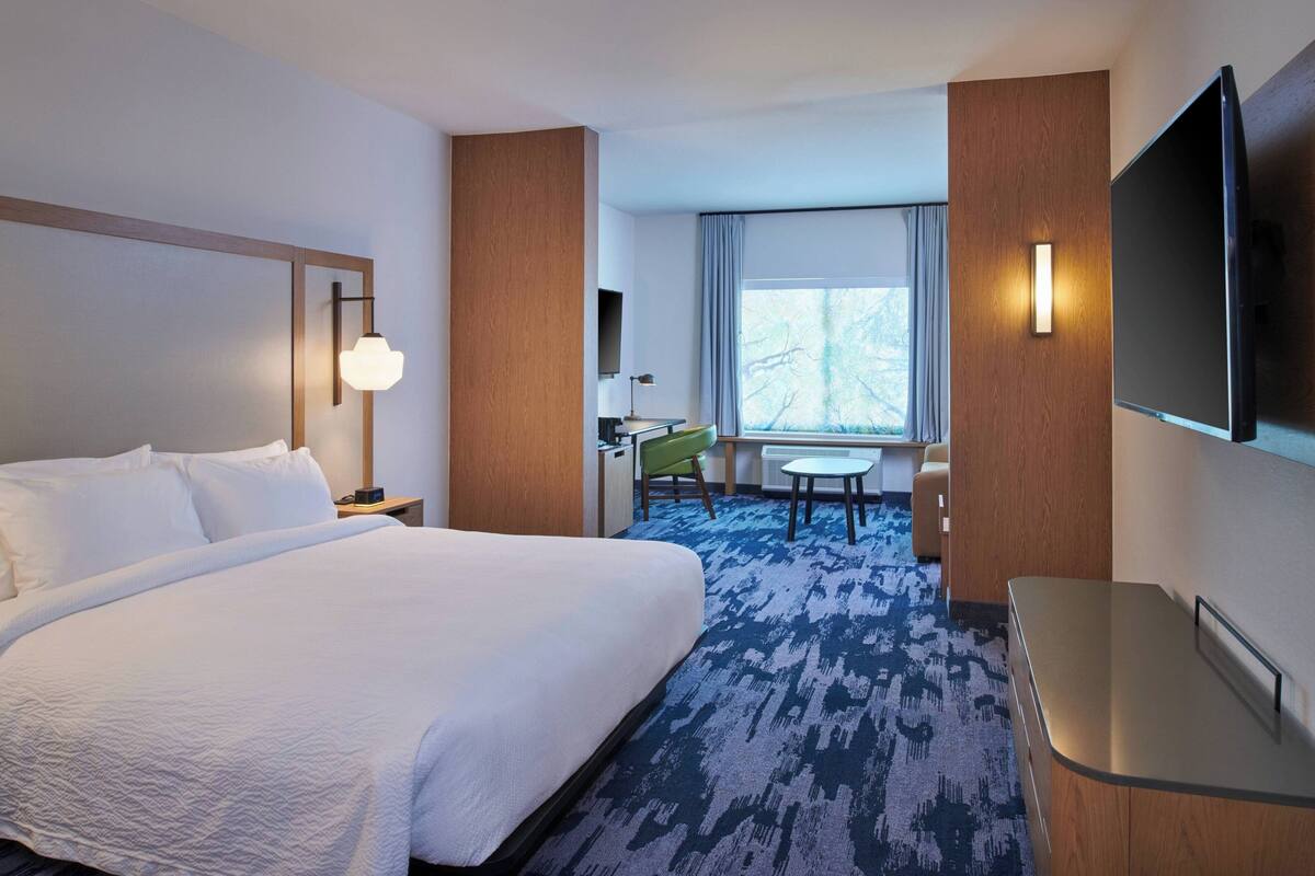 Une chambre d’hôtel avec un grand lit, un bureau, une chaise, une télévision et une fenêtre avec des rideaux.