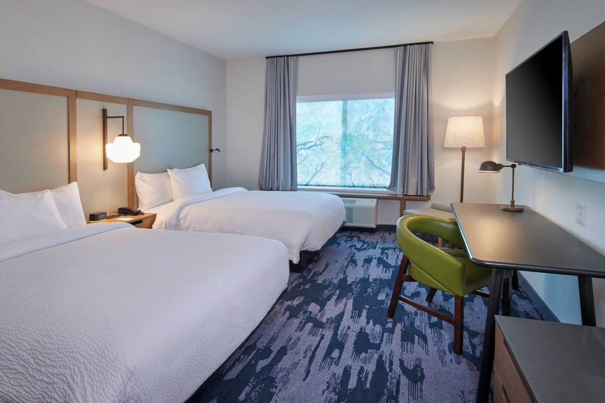 Une chambre d’hôtel avec deux lits, un bureau, une chaise, une télévision et une fenêtre avec des rideaux.