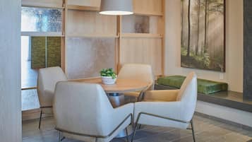 A modern dining area with a round table, four chairs, a pendant light, and a painting of a forest on the wall.