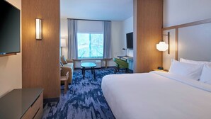 A hotel room with a bed, a desk, a chair, a TV, and a window with curtains.
