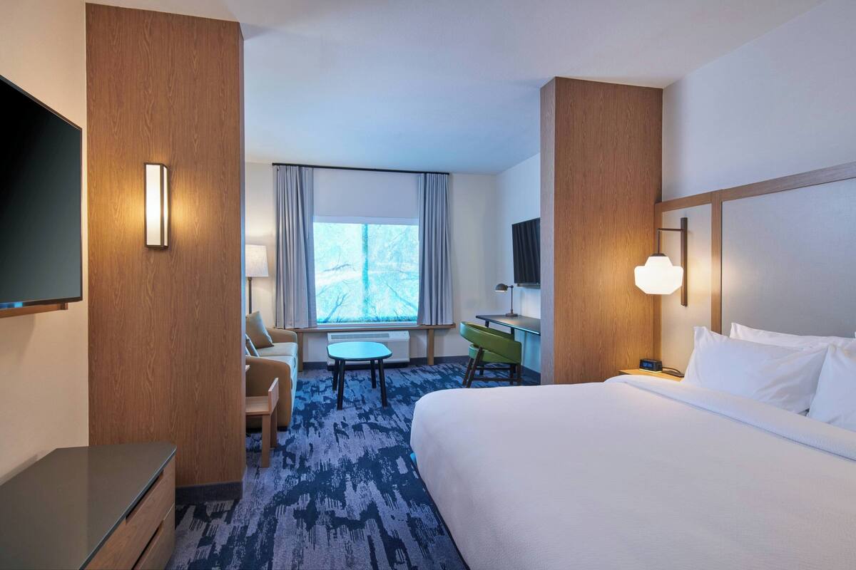 Une chambre d’hôtel avec un lit, un bureau, une chaise, une télévision et une fenêtre avec des rideaux.