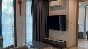 A modern living room with a flat-screen TV, a sofa, a coffee table, and a sliding glass door leading to a balcony. - Arcadia beach condo by Jiabo (Pattaya)