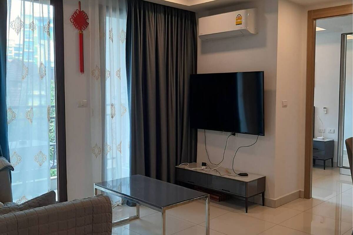 A modern living room with a flat-screen TV, a sofa, a coffee table, and a sliding glass door leading to a balcony.