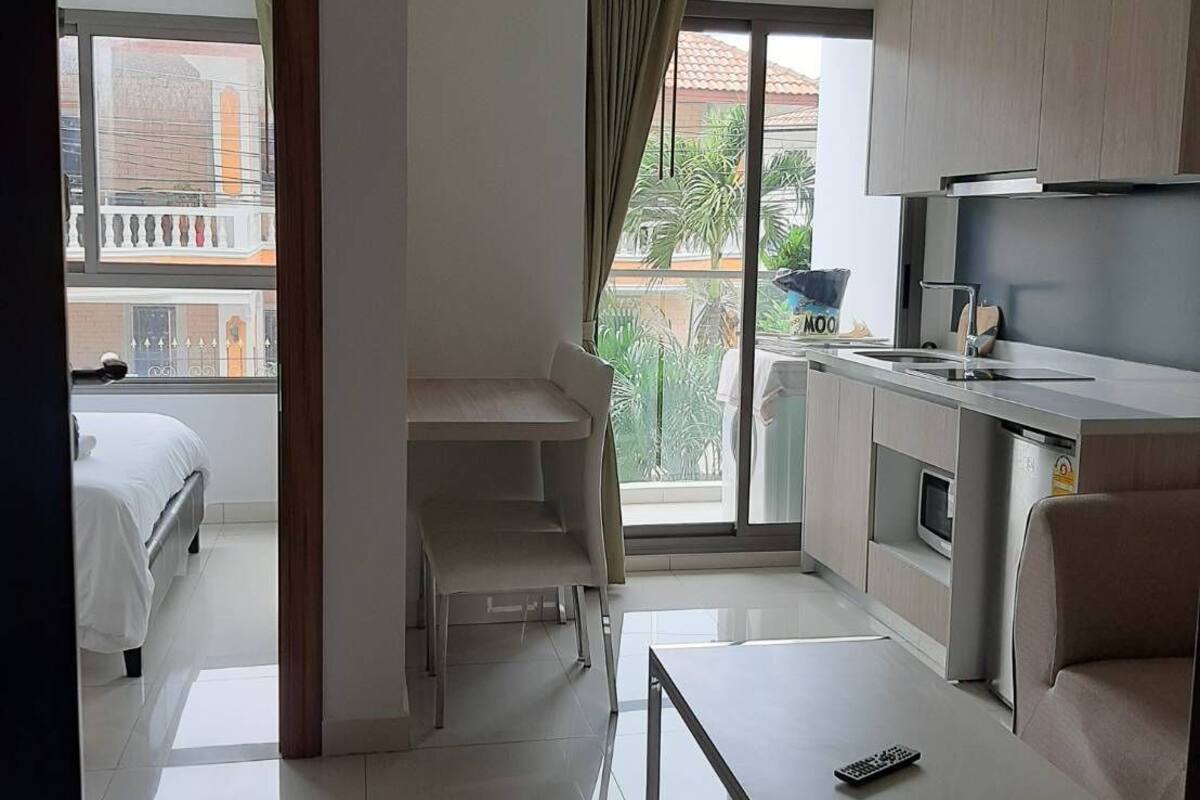 A modern hotel room with a balcony, a kitchenette, a dining area, and a separate bedroom.