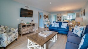 A living room with a blue sofa, a wooden coffee table, and a TV mounted on the wall.