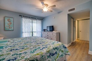 Un dormitorio con cama, ventilador de techo, ventana con cortinas, cómoda y puerta.