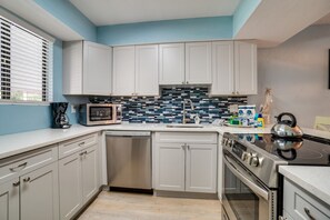Una cocina moderna con armarios blancos, lavavajillas de acero inoxidable, estufa negra y salpicadero de azulejos azules.