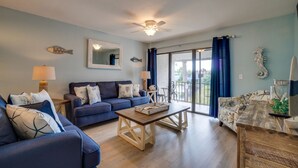 A living room with a blue sofa, a wooden coffee table, and a balcony with blue curtains.