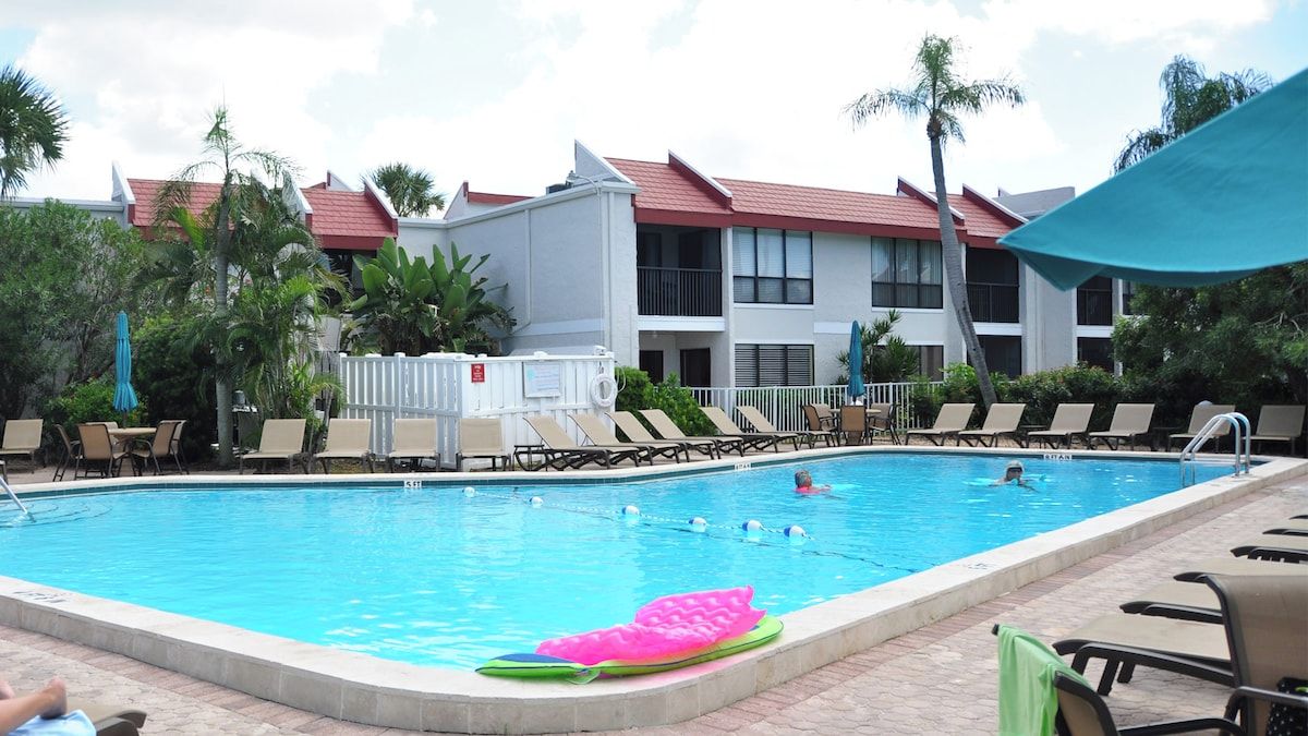 A swimming pool with lounge chairs and umbrellas, surrounded by buildings with red roofs.