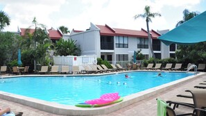 Una piscina con sillas de descanso y sombrillas, rodeada de edificios con tejados rojos.