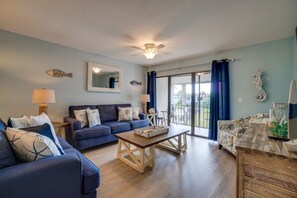 A living room with a blue sofa, a wooden coffee table, and a balcony with a view.
