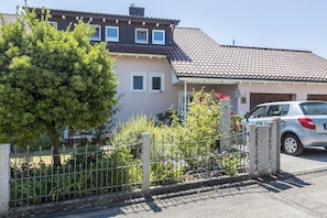 Et bolighus med tegltag, en indhegnet have og en parkeret bil.
