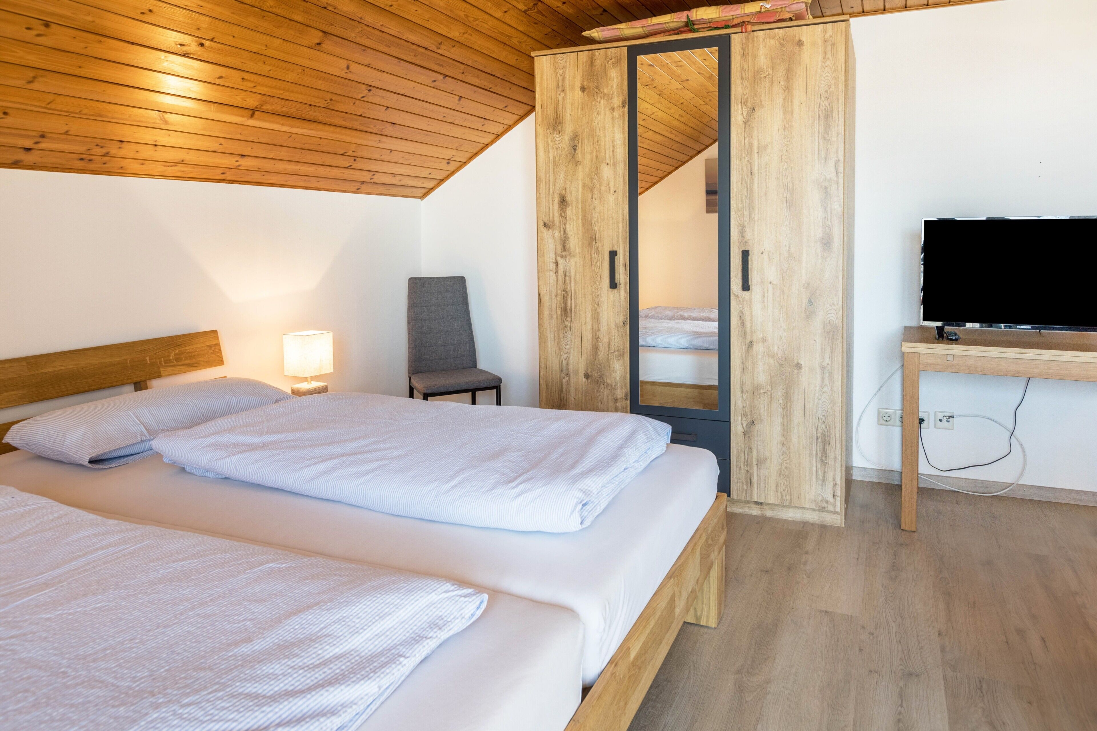 A bedroom with two beds, a desk, a chair, and a TV.