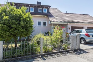 Une maison d’habitation avec un toit en tuiles, un jardin clôturé et une voiture garée.