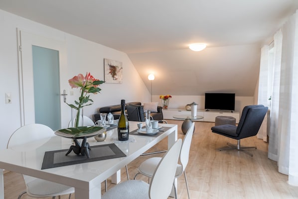 A modern living room with a dining area, a flat-screen TV, and a sofa.