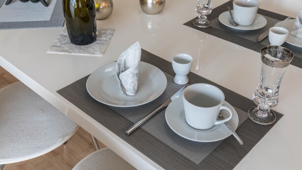 Een net gedekte eettafel met borden, bekers en een fles, compleet met placemat en servet.