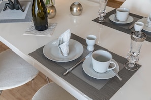 A neatly set dining table with plates, cups, and a bottle, accompanied by a placemat and a napkin.