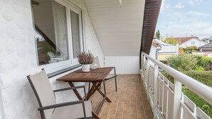 Een balkon met een houten tafel en stoelen, een plant in pot, en uitzicht op een woonwijk.