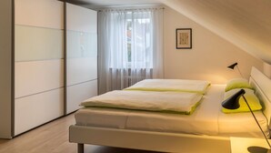 Een slaapkamer met een bed, bedlampen, een raam met gordijnen en een ingelijst schilderij aan de muur.