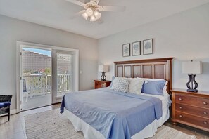 Quarto com uma cama grande, uma mesa de cabeceira de madeira, um ventilador de teto e uma varanda com vista.