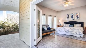 A bedroom with a bed, a nightstand, a lamp, a ceiling fan, and a view of the outdoors.