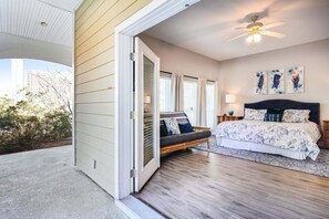 A bedroom with a bed, a nightstand, a lamp, a ceiling fan, and a view of the outdoors.
