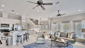 A spacious living area with a central seating arrangement, a kitchen with modern appliances, and a staircase leading to an upper level.