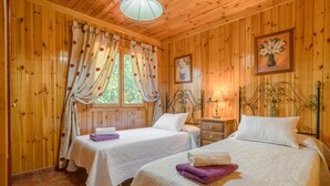 Ein Zimmer mit Holzwänden, zwei Betten, einem Nachttisch und einem Fenster mit Vorhängen.